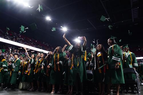 Group of graduates wearing green regalia and tossing their caps in the air to celebrate!