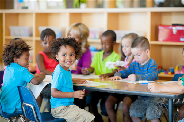 Young children seating on a table coloring, one smiles at the camera
